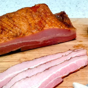 black honey cured bacon - whole and slices on a wooden board