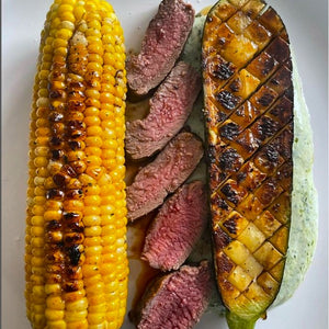 Cooked sweetcorn, lamb and a half courgette with black honey charring on a plate/