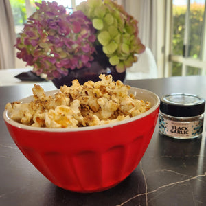 a bowl of black honey popcorn with black garlic salt sprinkles also visible