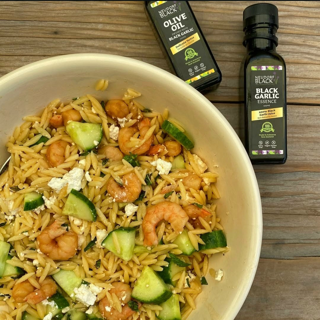 bowl with prawns, orzo, cucumber salad and a bottle of Black Garlic Essence beside the bowl.