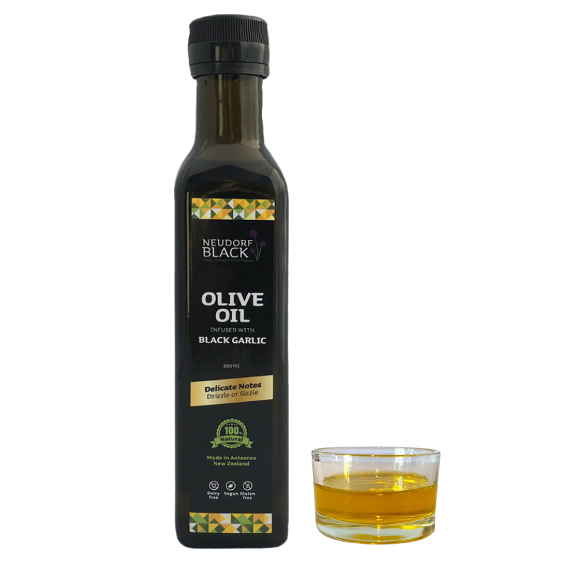 A bottle of Black Garlic infused olive oil next to a small glass dish containing the infused oil, on a white background.
