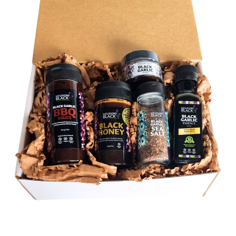 Collection of black garlic products in a box with brown tissue paper - one is original Black Honey in a squeezy tube