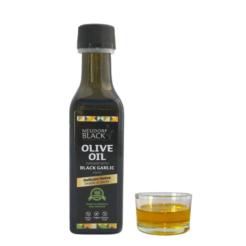 A bottle of olive oil infused with black garlic next to a small glass dish containing the infused oil, on a white background.