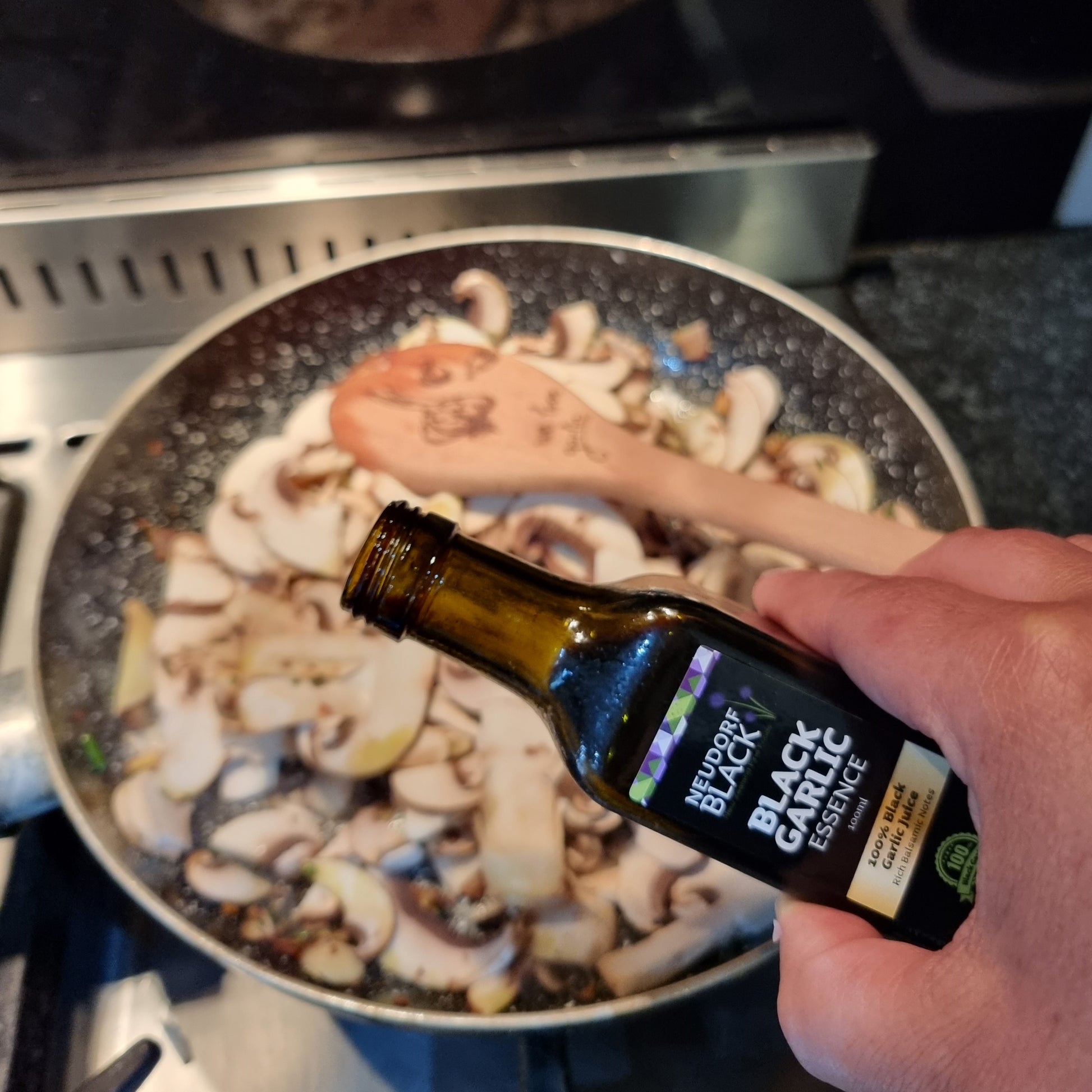 Black Garlic Essence being poured on mushrooms in a fry pan
