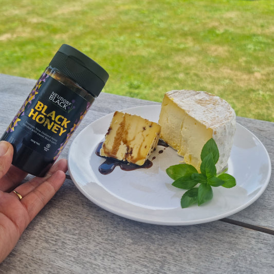tube of Black Honey beside a plate with a cheese cheese wedge with black honey drizzled over it.