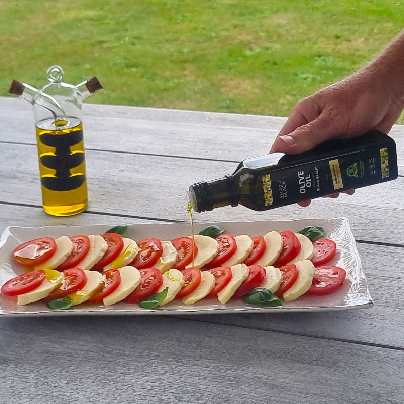 Black Garlic olive oil from Neudorf Black being poured over a salad on a wooden table.