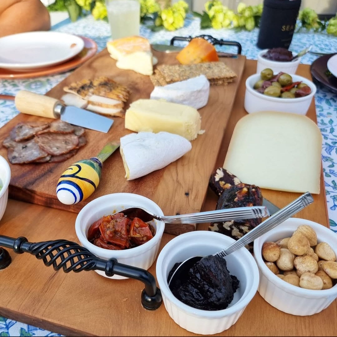 A wooden board with an assortment of cheeses and pickles with Black Garlic Puree in a ramekin ready to use