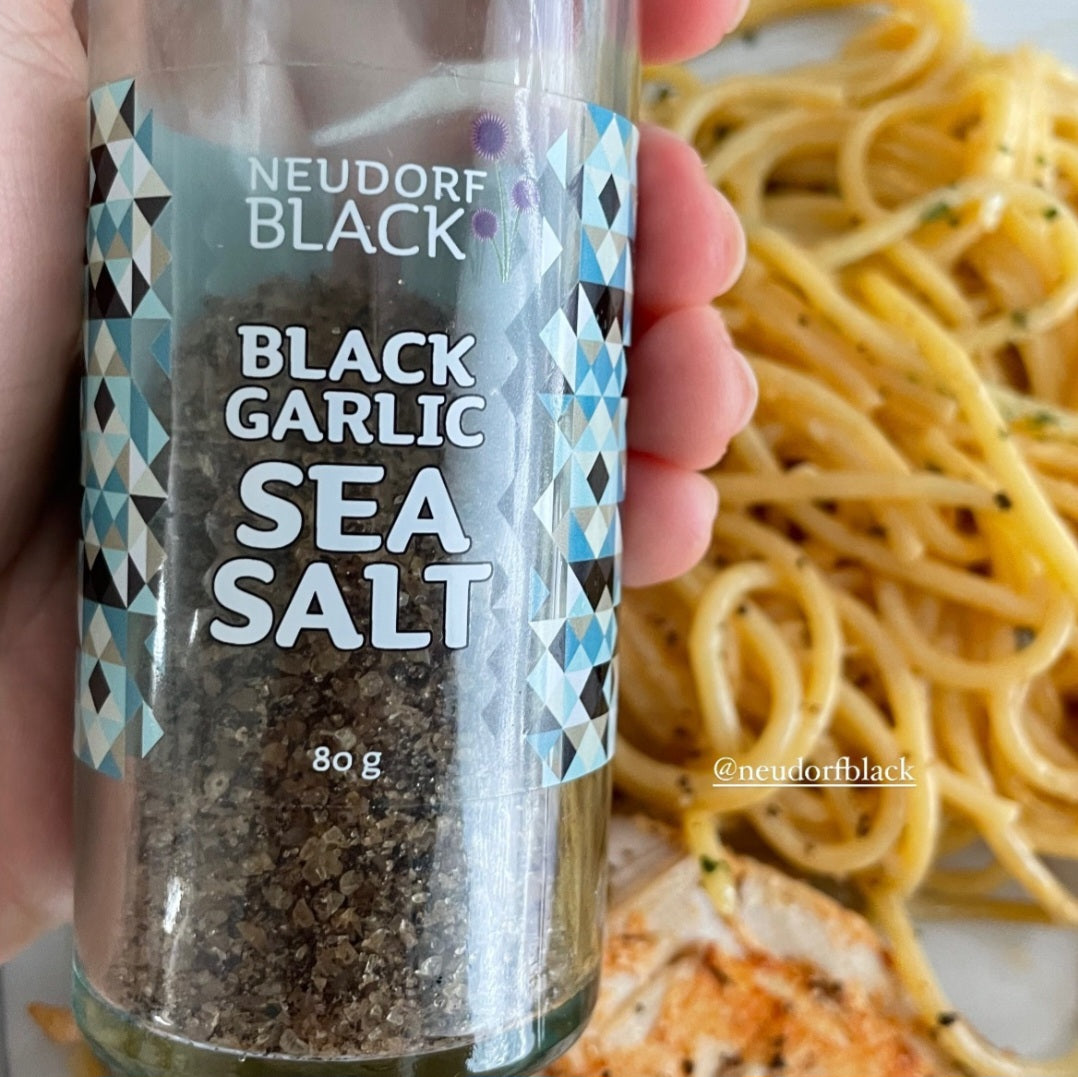Neudorf Black Garlic Sea Salt in reusable 80g glass shaker above a plate of spaghetti and chicken - Marlborough Sea Salt blended with black garlic powder