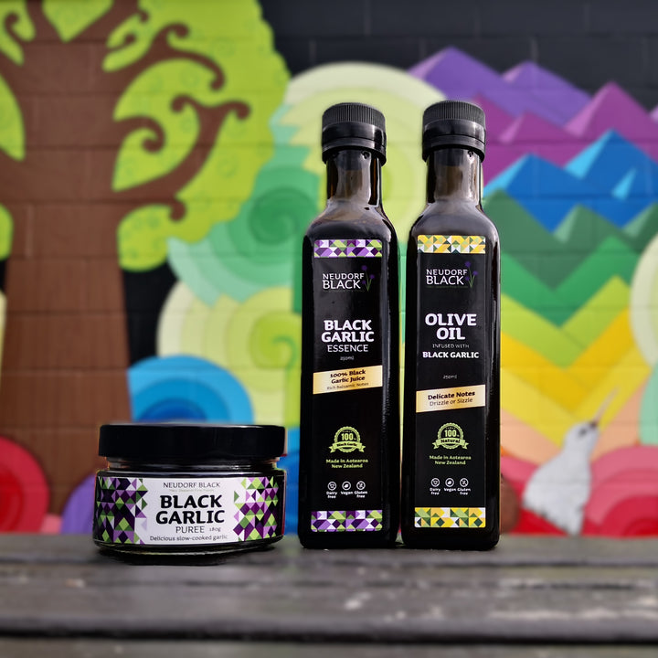 A jar of black garlic puree beside a bottle of Essence and Black Garlic Olive oil against a colourful background