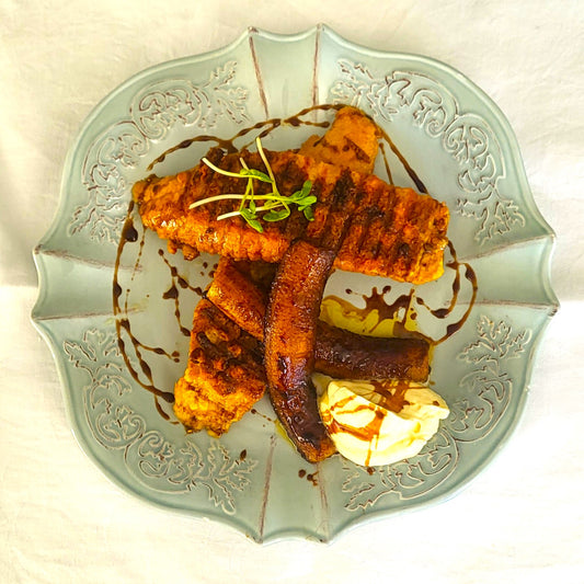 Black honey drizzled over french toast and grilled banana on a plate with whipped cream.