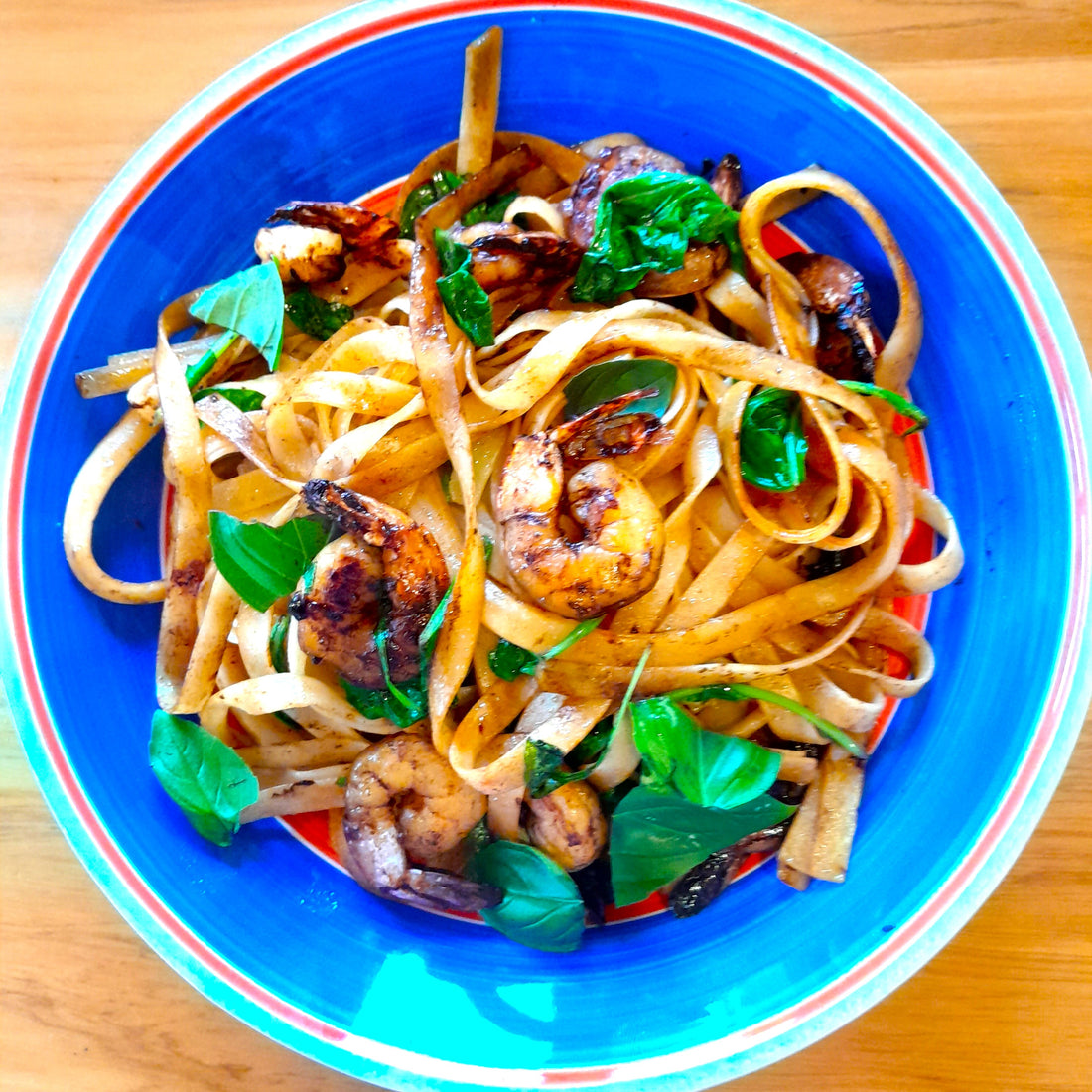 pasta topped with prawns and greens in a colourful bowl