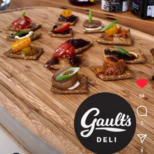 Square black garlic crackers with morsels of chutney and tomatoes on top arranged on a wooden board