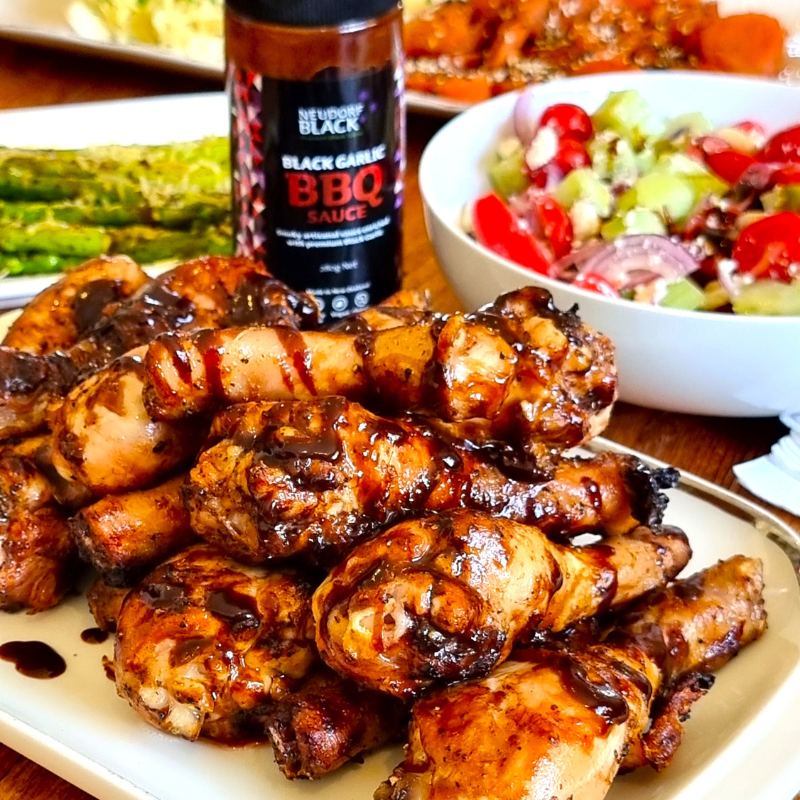 Bottle of Black Garlic BBQ Sauce beside a plate stacked high with BBQ chicken drumsticks
