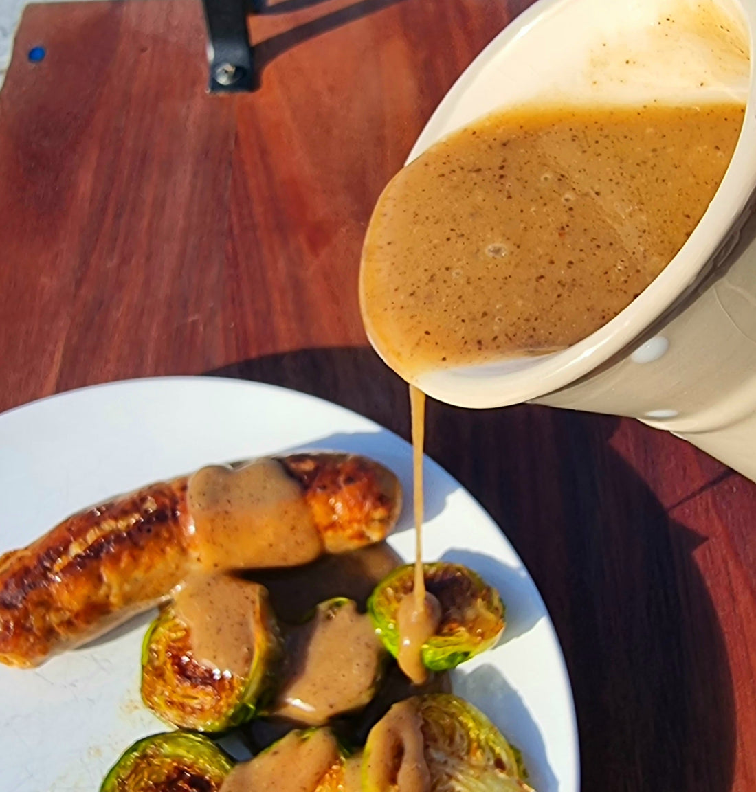 Black garlic gravy pouring over brussel sprouts and sausage