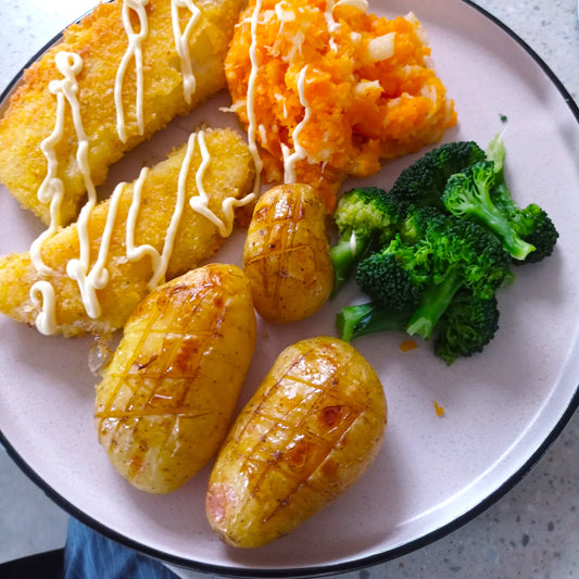 Black Honey and Butter Potatoes on a dish with broccoli, mash and fish fillets.