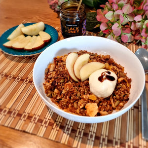 bowl filled with granola and sliced apples on top with dollop of yoghurt that has Black Honey drizzled over.
