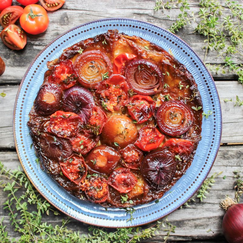 A whole tarte tatin filled with cooked tomatoes and red onions on a plate