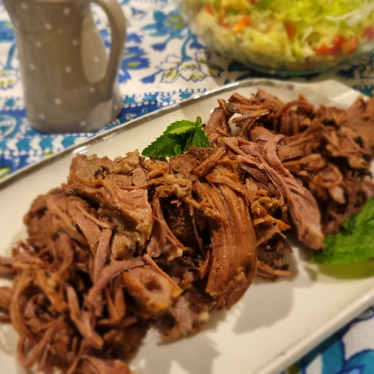 Shredded lamb on a plate beside a gravy boat