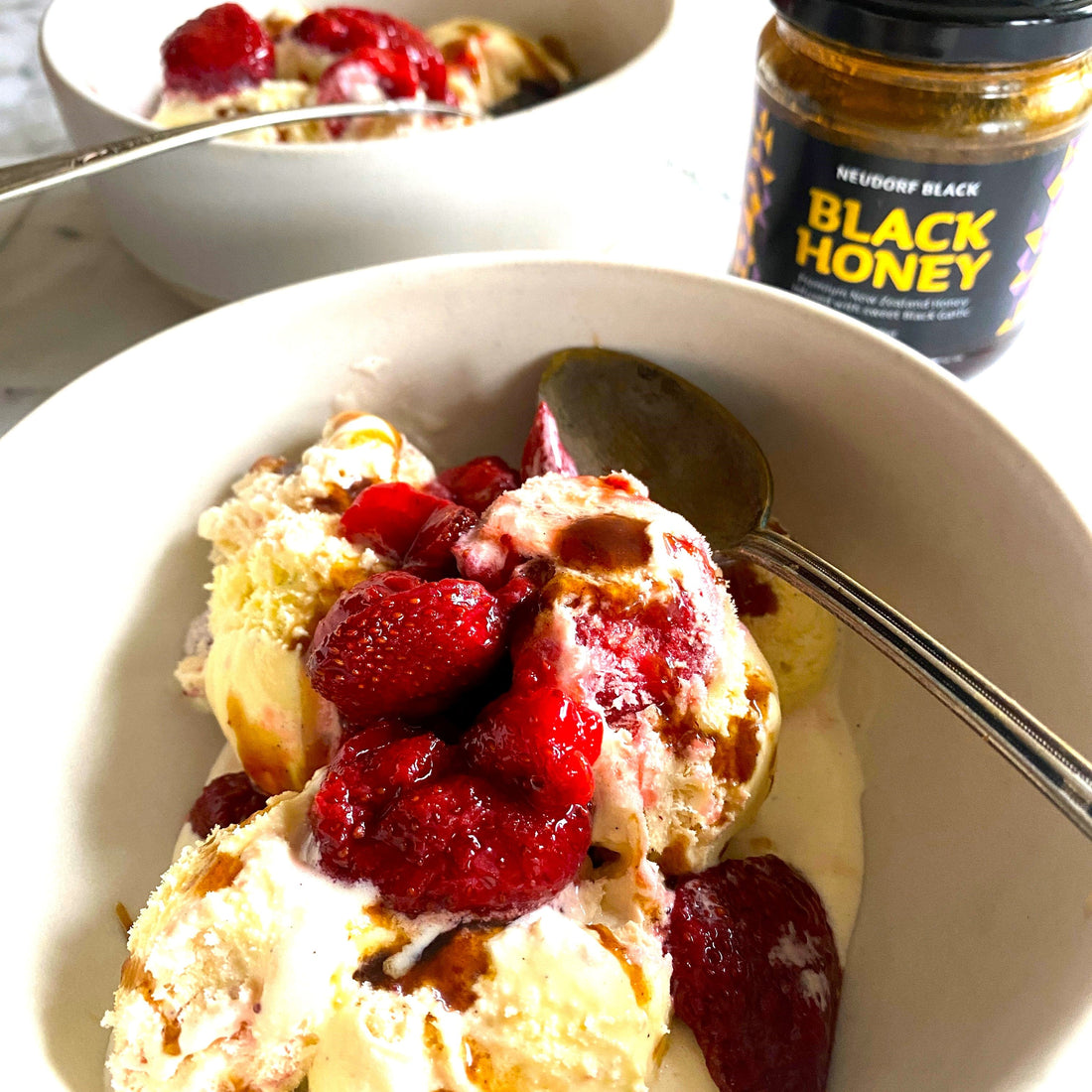 plate of icecream with strawberries on top and jar of Black Garlic Honey beside.