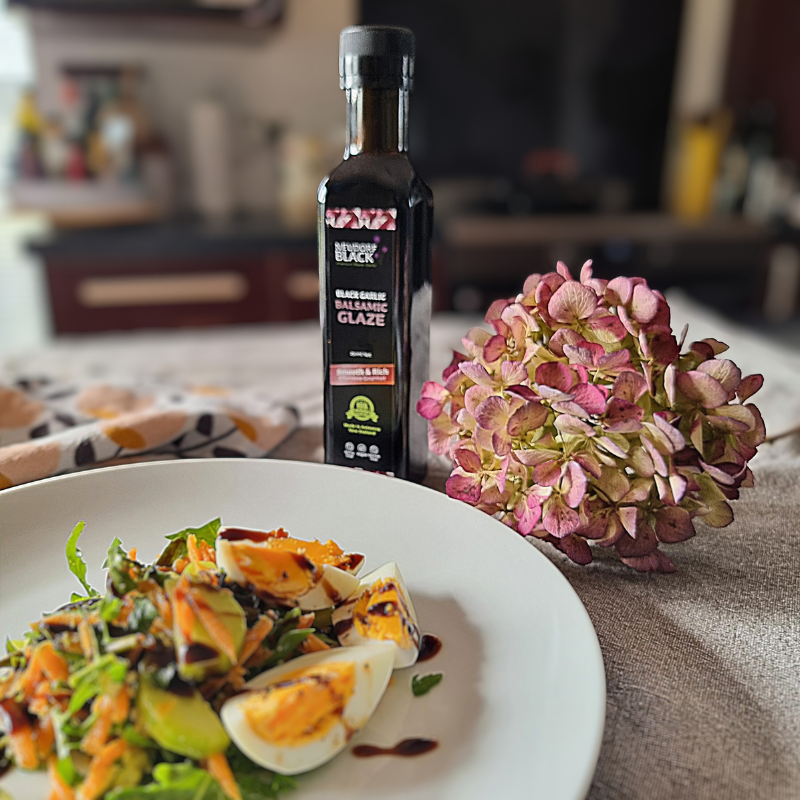 Neudorf Black Balsamic Glaze bottle on a table with a salad and flowers