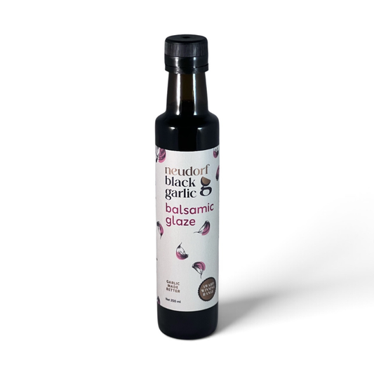 A bottle of Neudorf Black Garlic Balsamic Glaze on a clean white background. The product is in a dark glass bottle with a black cap and a white label featuring illustrations of garlic cloves.