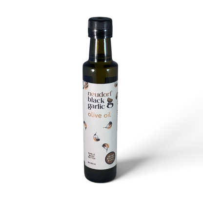 A bottle of Neudorf Black Garlic Olive Oil on a clean white background. The dark glass bottle features a black cap and a white label with illustrations of garlic cloves and text reading 'neudorf black garlic olive oil'.
