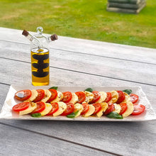 A dual chamber glass decanter filled with Neudorf Black Olive Oil and Neudorf Black Garlic Essence sits beside a plate of fresh mozzarella cheese and tomato